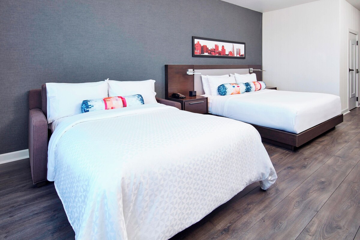 A hotel room with two beds, a cityscape artwork on the wall, and a wooden floor.