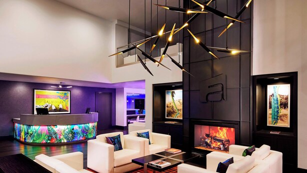 A modern lobby with a reception desk, white sofas, a fireplace, and a large TV screen. - Aloft by Marriott San Jose Cupertino (San Jose)