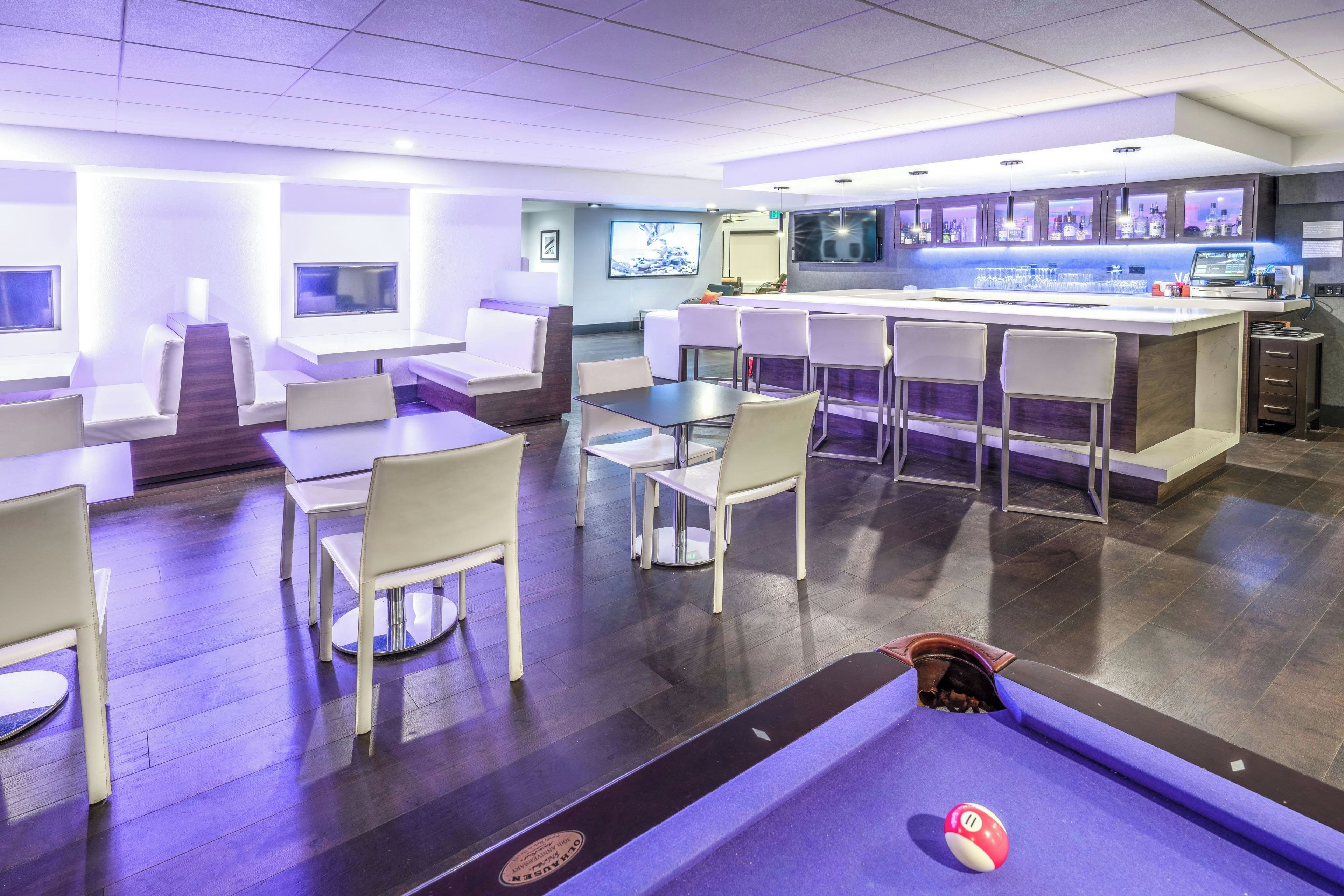 A modern bar area with seating, a pool table, and a bar counter with a digital screen.