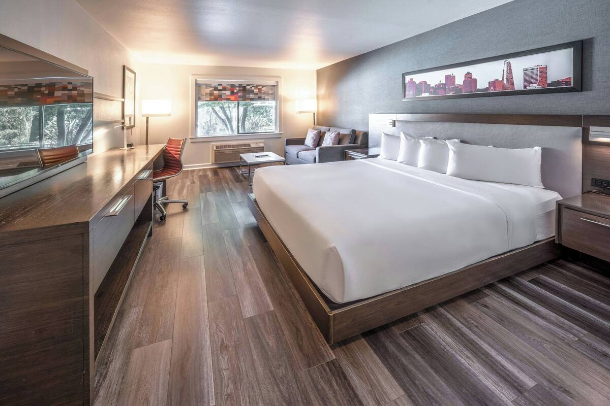 A modern hotel room with a large bed, a desk, and a seating area.