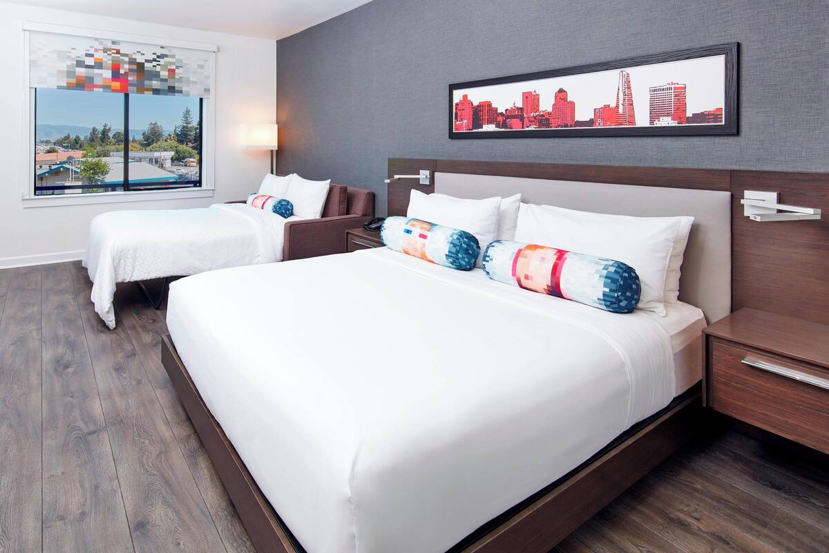 A hotel room with two beds, a cityscape view, and a framed city skyline picture on the wall.