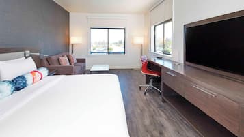 A hotel room with a large bed, a sofa, a desk with a TV, and a window with a view.