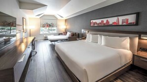 A modern hotel room with a large bed, a desk, and a chair. There is a cityscape painting on the wall and a window with a view. - Aloft by Marriott San Jose Cupertino (San Jose)