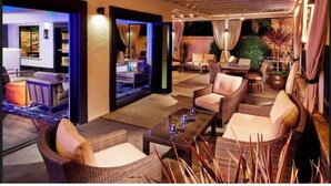 A well-lit outdoor lounge area with wicker furniture, a coffee table, and a potted plant. - Aloft by Marriott San Jose Cupertino (San Jose)