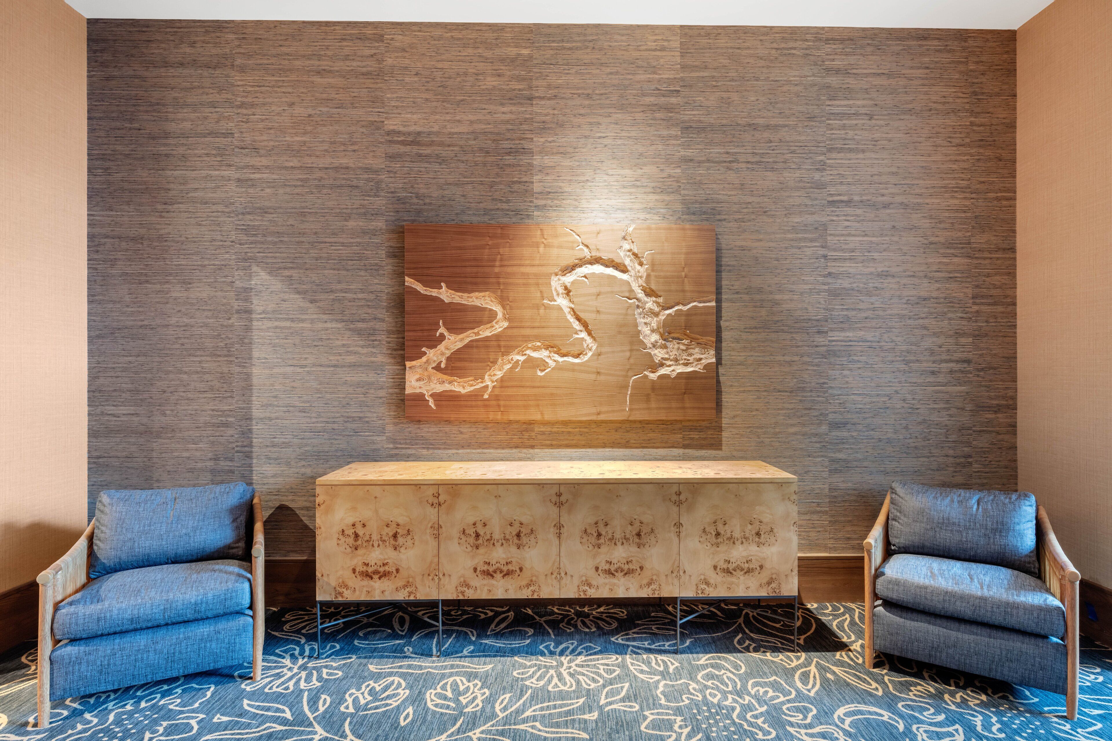 A room with a modern design, featuring a wooden textured wall, a central console table, and two matching armchairs.