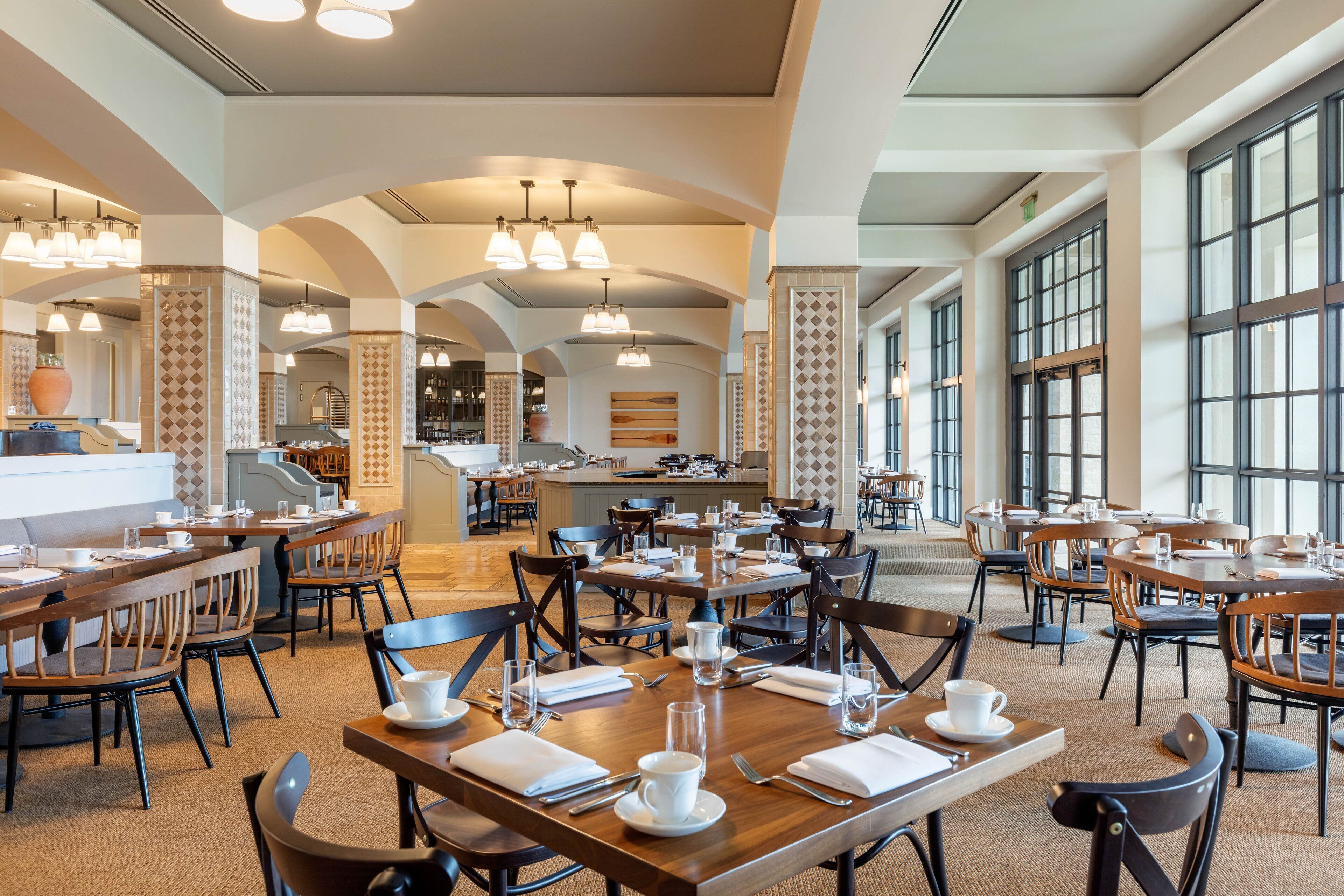 A spacious dining area with multiple tables and chairs, large windows, and a central island with a kitchen.