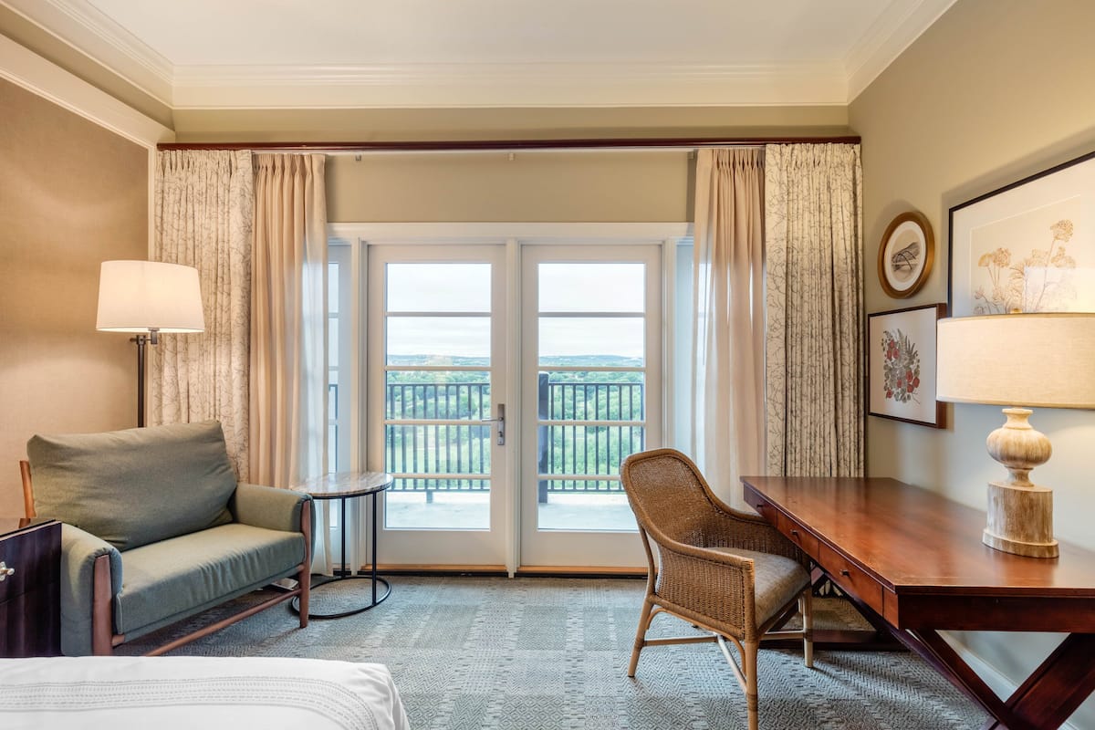Ein Hotelzimmer mit Bett, Sofa, Sessel, Schreibtisch, Lampe, kleinen Tisch und einem Balkon mit Blick.