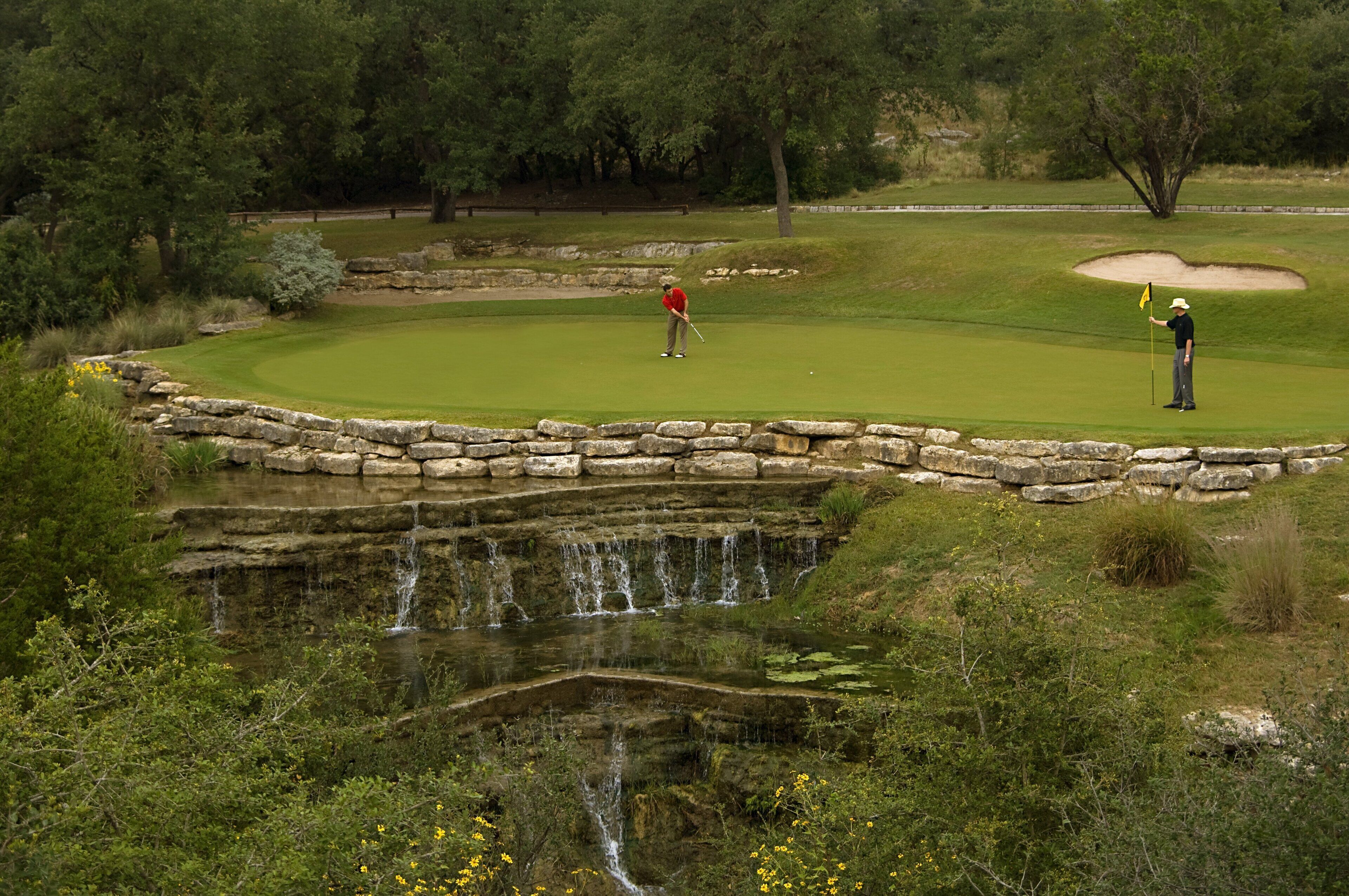 A golf course with a pond, stone walls, and trees.