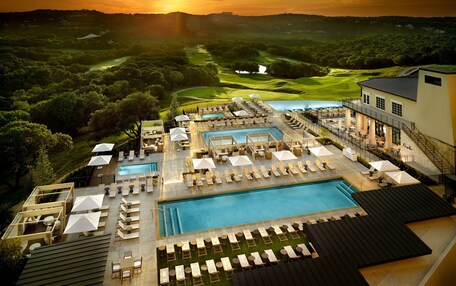 A resort with multiple swimming pools, sun loungers, and a golf course in the background.
