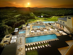 Un resort con varias piscinas, tumbonas y un campo de golf al fondo.