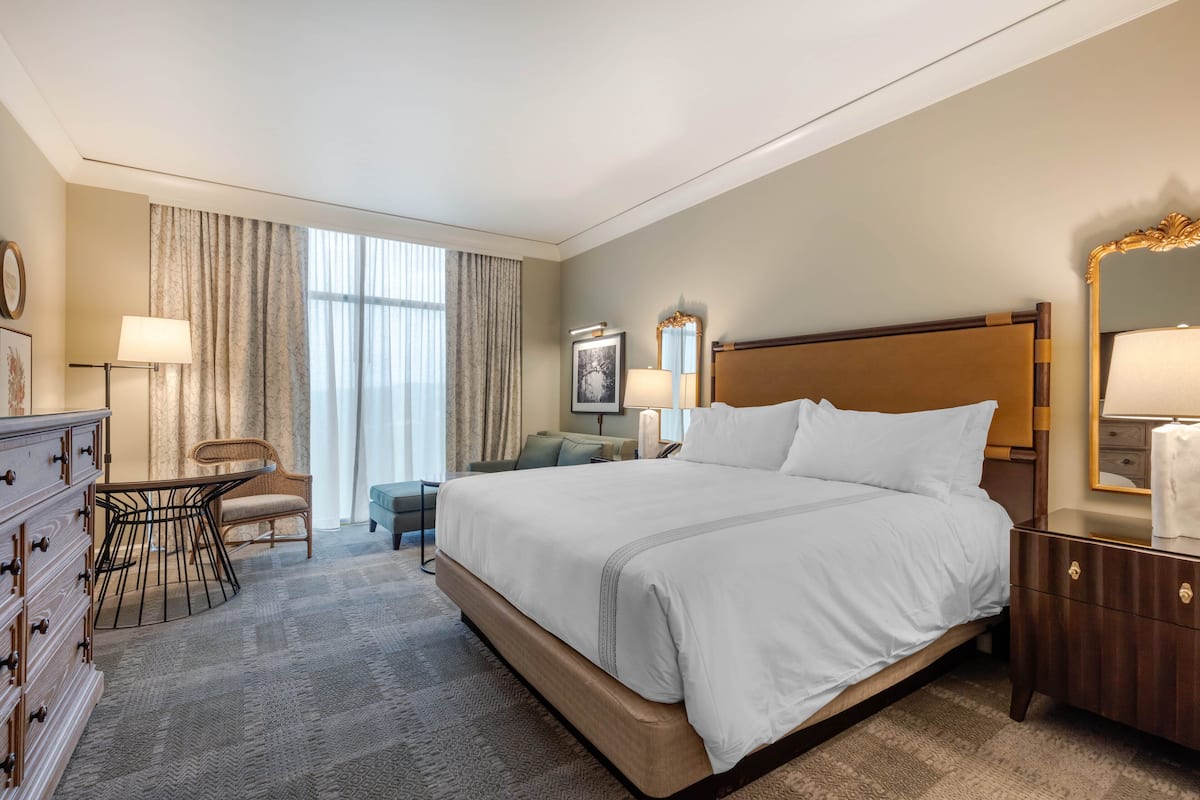 Ein Hotelzimmer mit einem großen Bett, einem Schreibtisch, einem Sessel, einer Kommode und einem Spiegel.