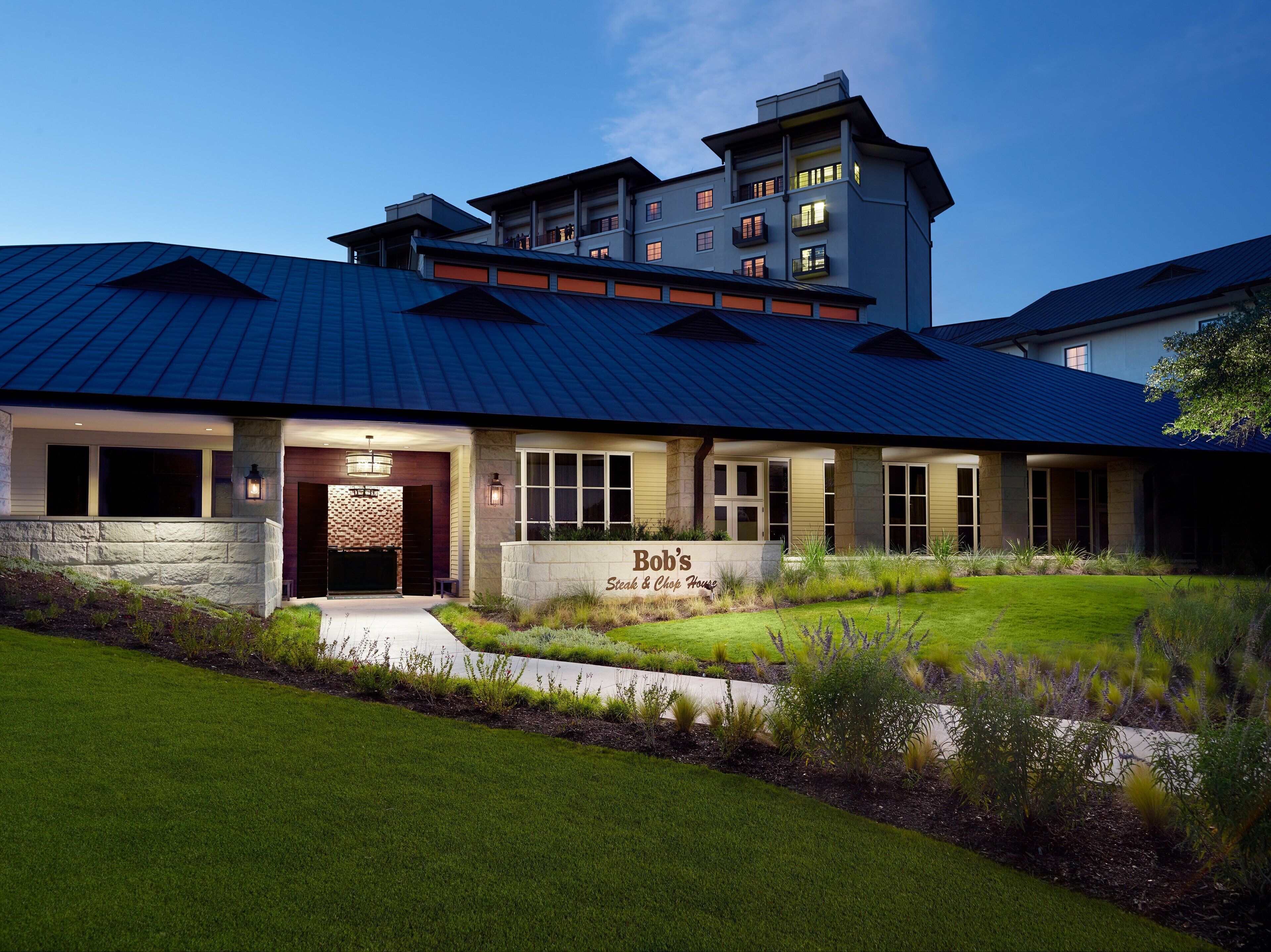 A steak and chop house with a stone facade, large windows, and a well-maintained lawn.