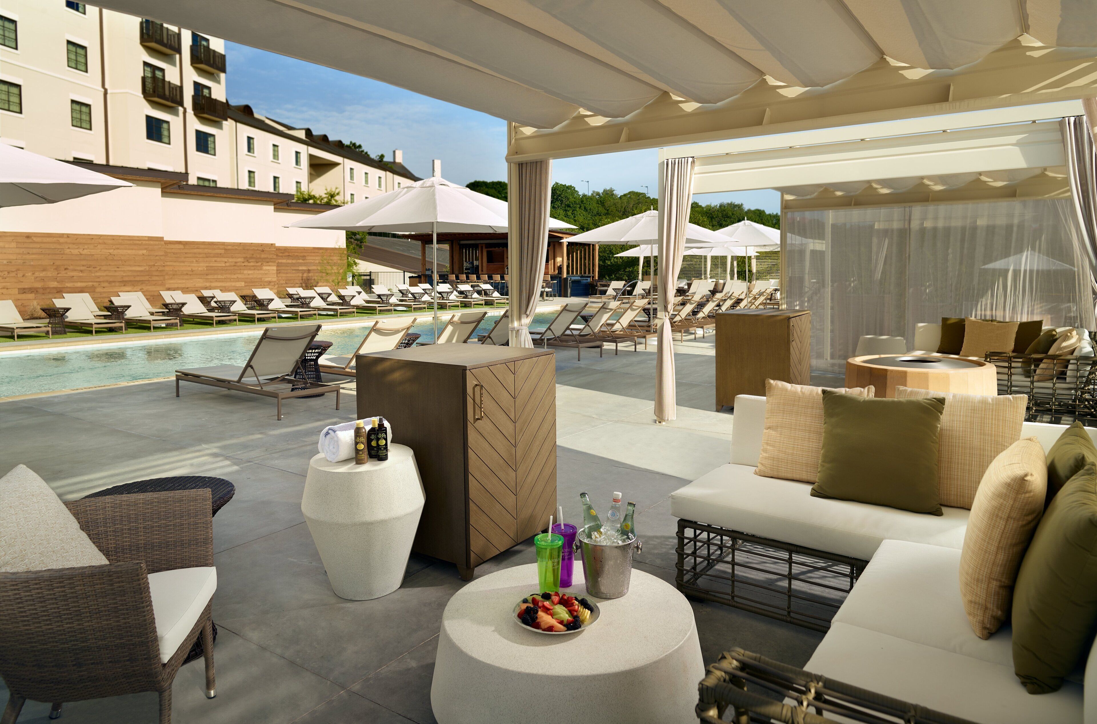 A poolside area with lounge chairs, umbrellas, and a buffet table with fruits and drinks.