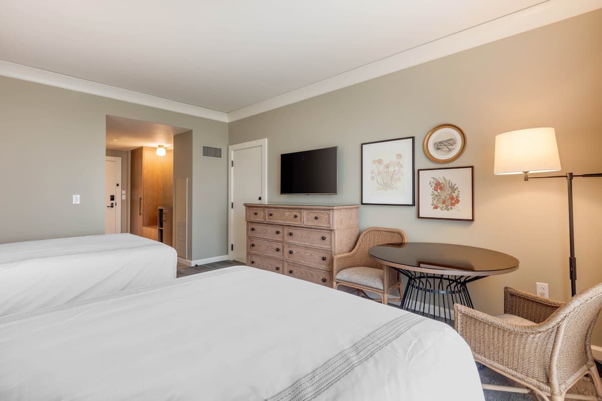 Ein Hotelzimmer mit zwei Betten, einem Schminktisch, einem Fernseher, einem Tisch mit Stühlen und Bildern an der Wand.