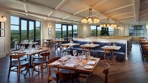 A restaurant with wooden tables and chairs, large windows offering views of the outdoors, and a central bar area. - Omni Barton Creek Resort & Spa Austin (Austin)