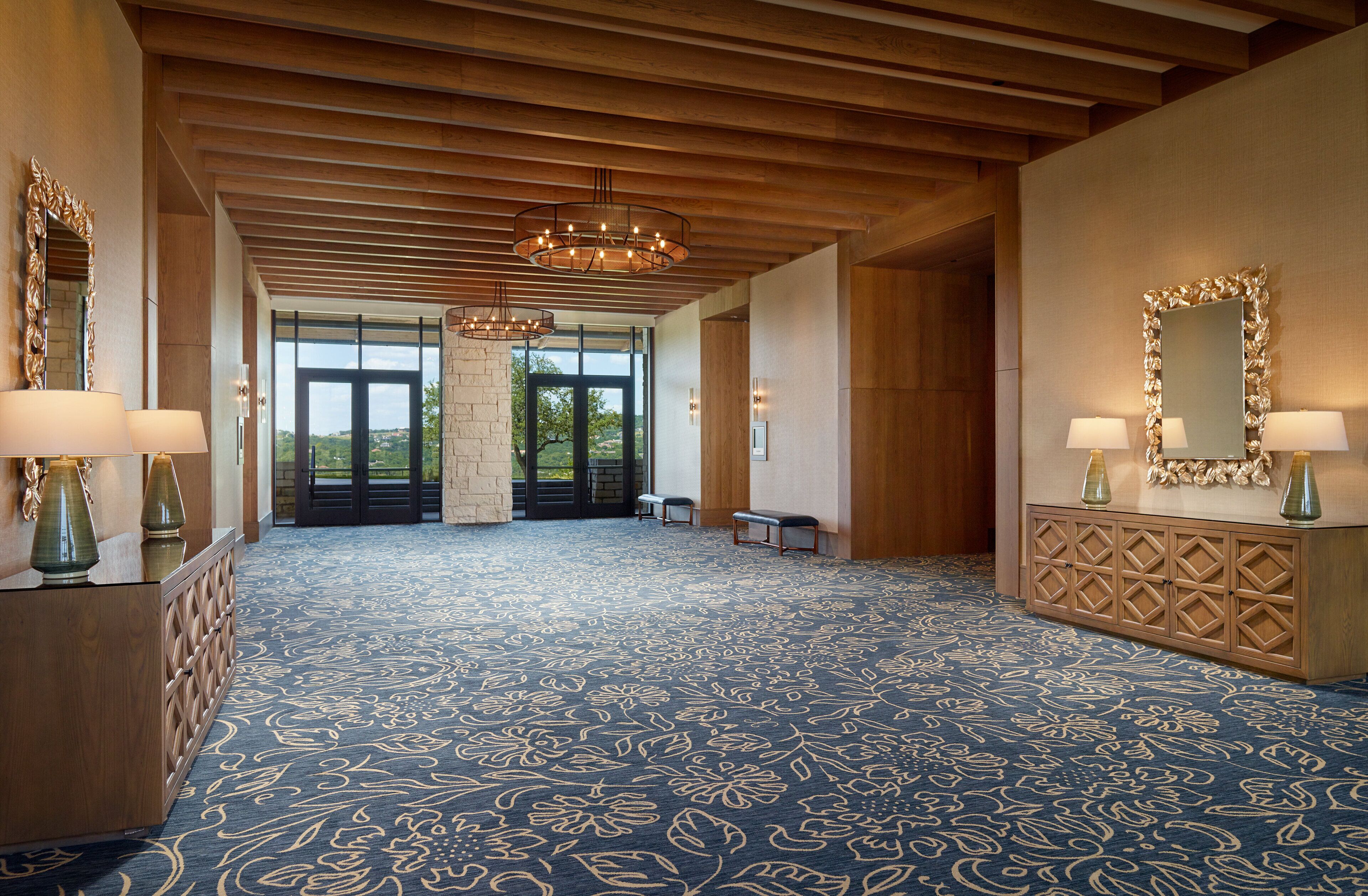 A spacious lobby with a patterned carpet, wooden ceiling beams, and a large mirror with lamps.