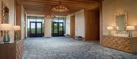 A spacious lobby with a patterned carpet, wooden ceiling beams, and a large mirror with lamps.