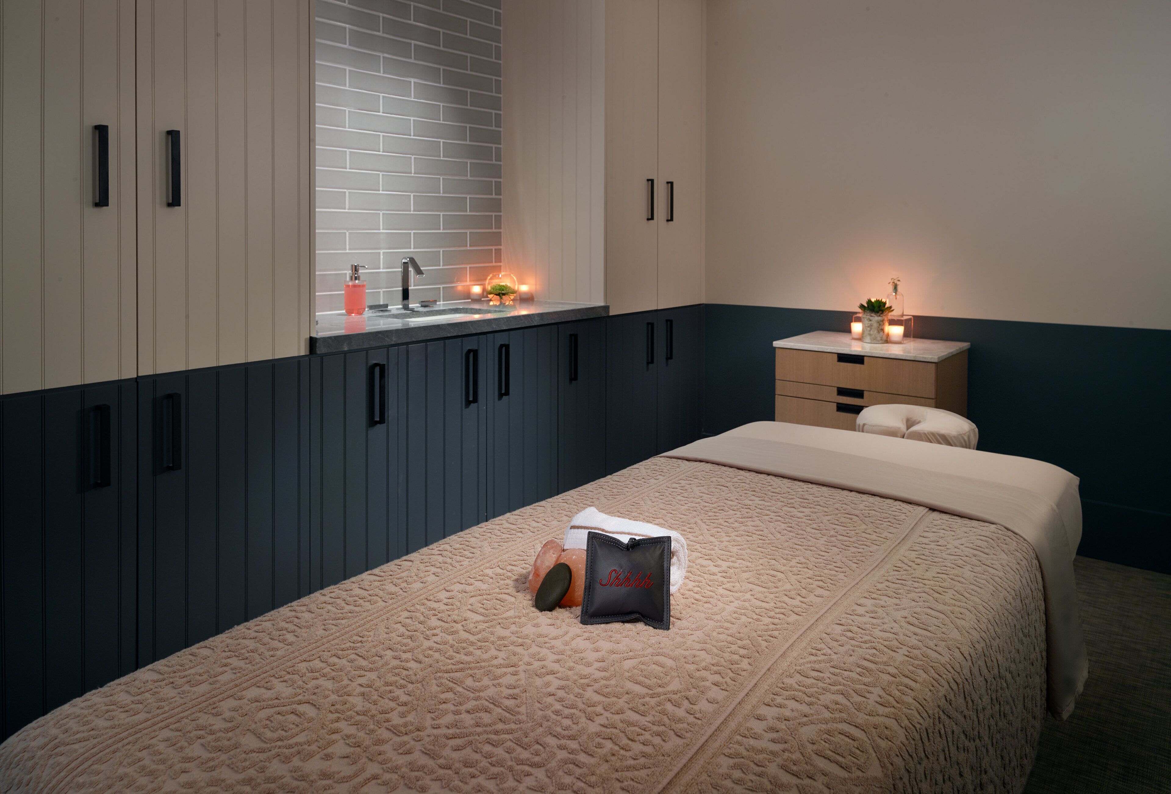 A bedroom with a bed, a nightstand, a dresser, and a window with a brick wall.