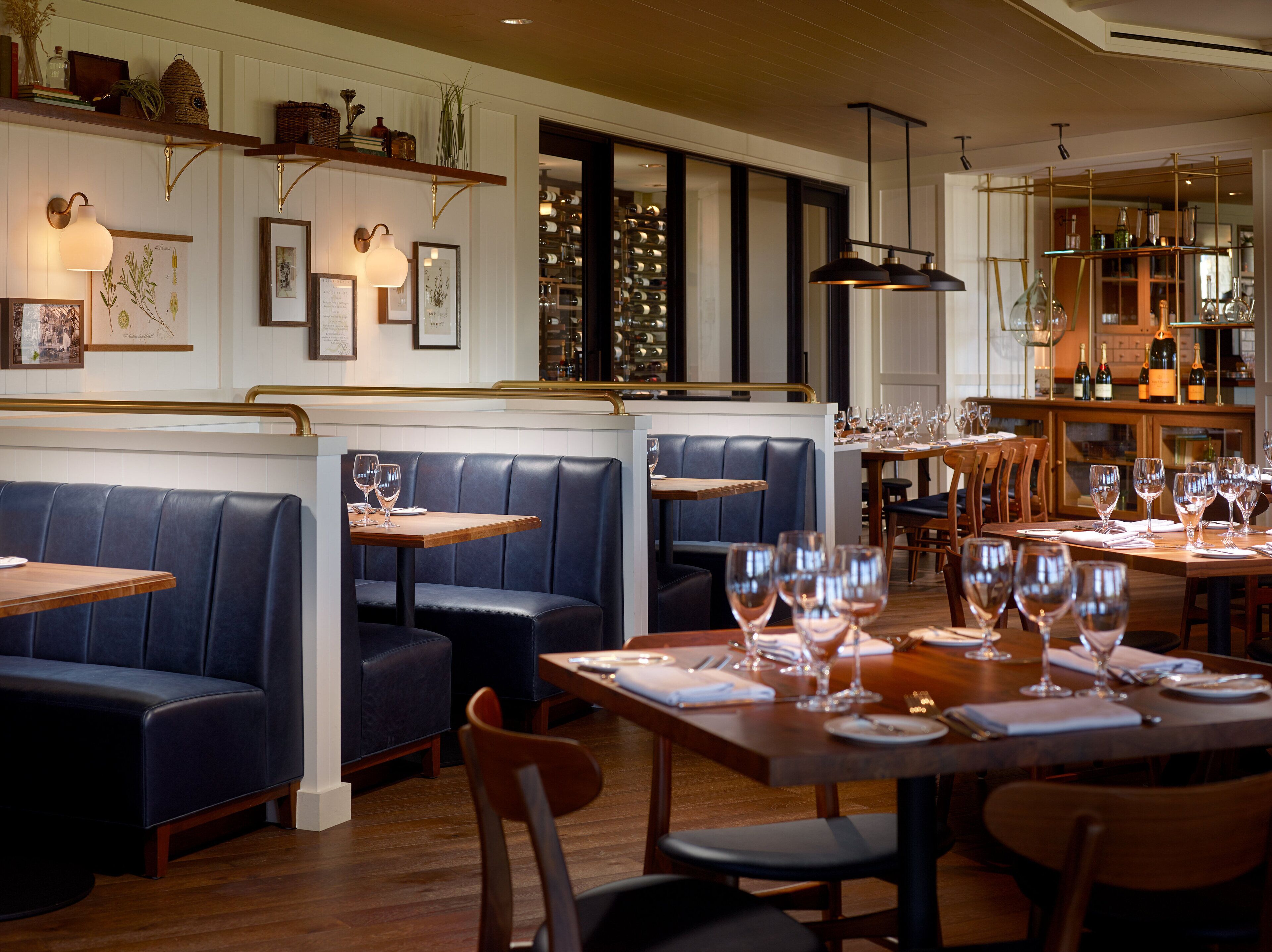 A restaurant interior with booths and tables, wooden flooring, and wall-mounted lighting.