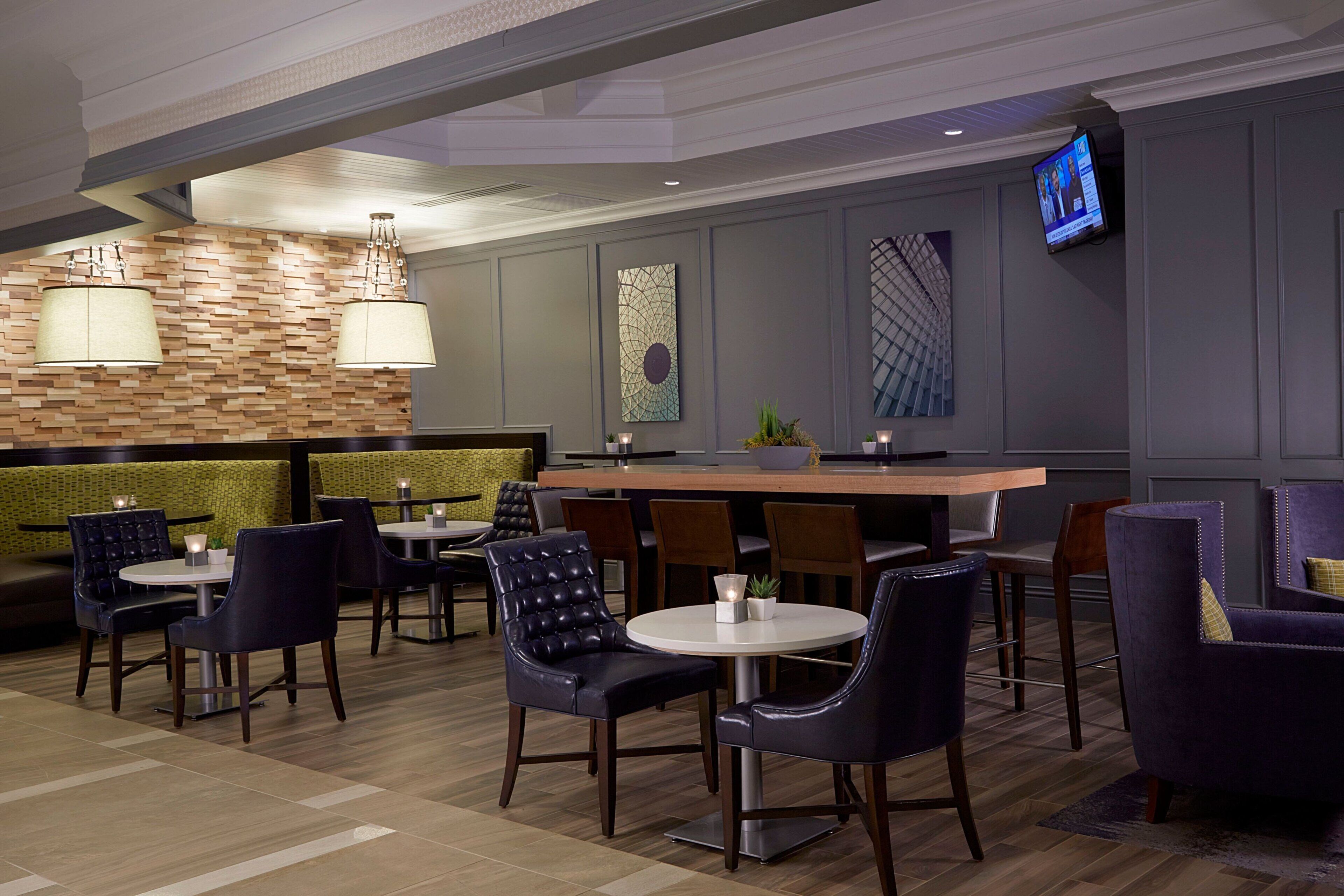 Un hall d’hôtel moderne doté d’un bar, de différents espaces de détente et d’un écran de télévision.