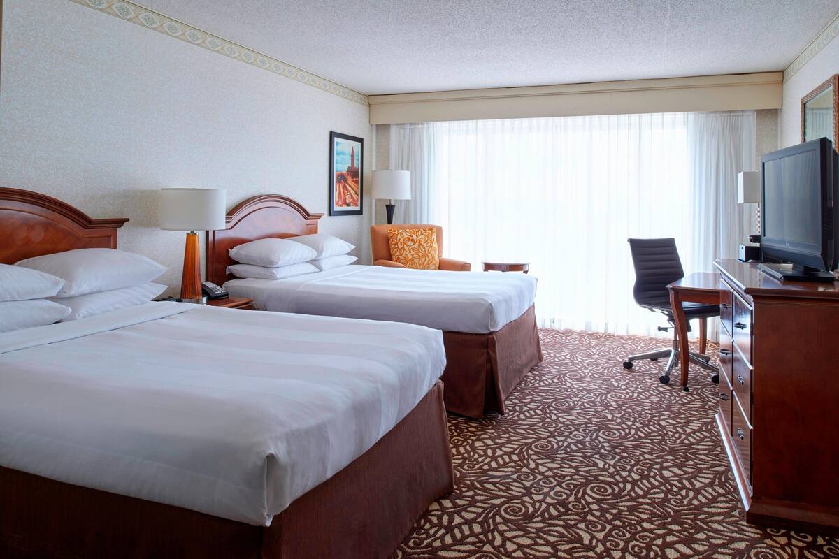 A hotel room with two beds, a television, a desk, and a chair.