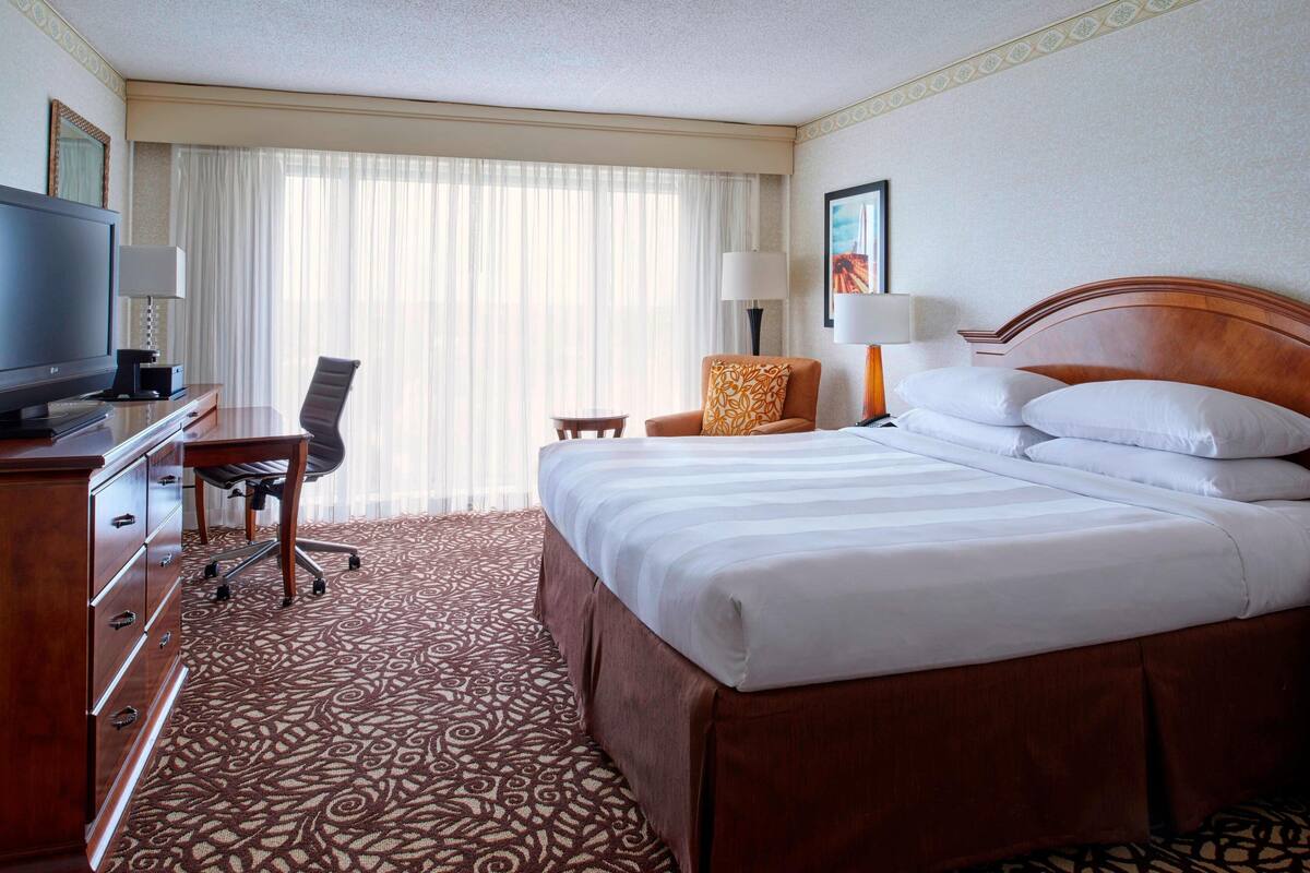 A hotel room with a large bed, a desk with a television, a chair, and a small table.