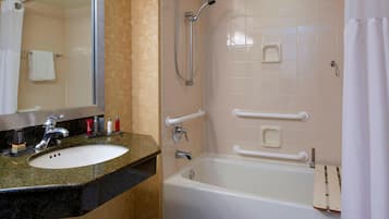 A bathroom with a sink, mirror, shower, and grab bars.