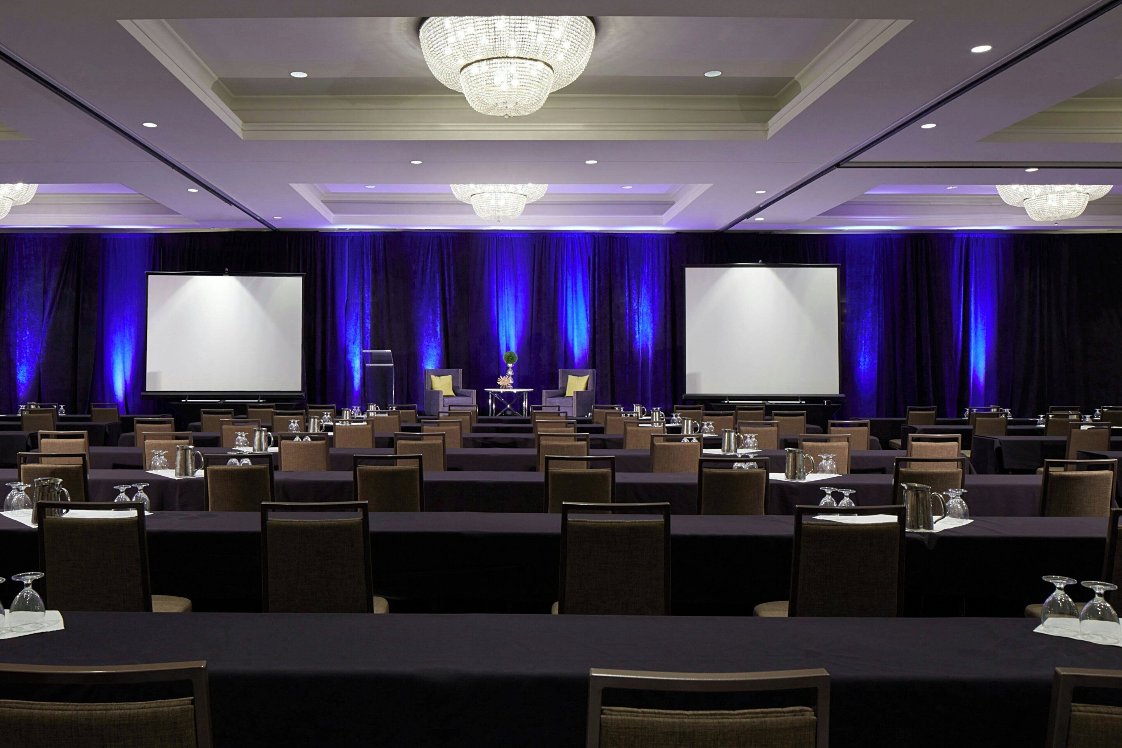A conference room with rows of tables, chairs, and a stage with a screen.
