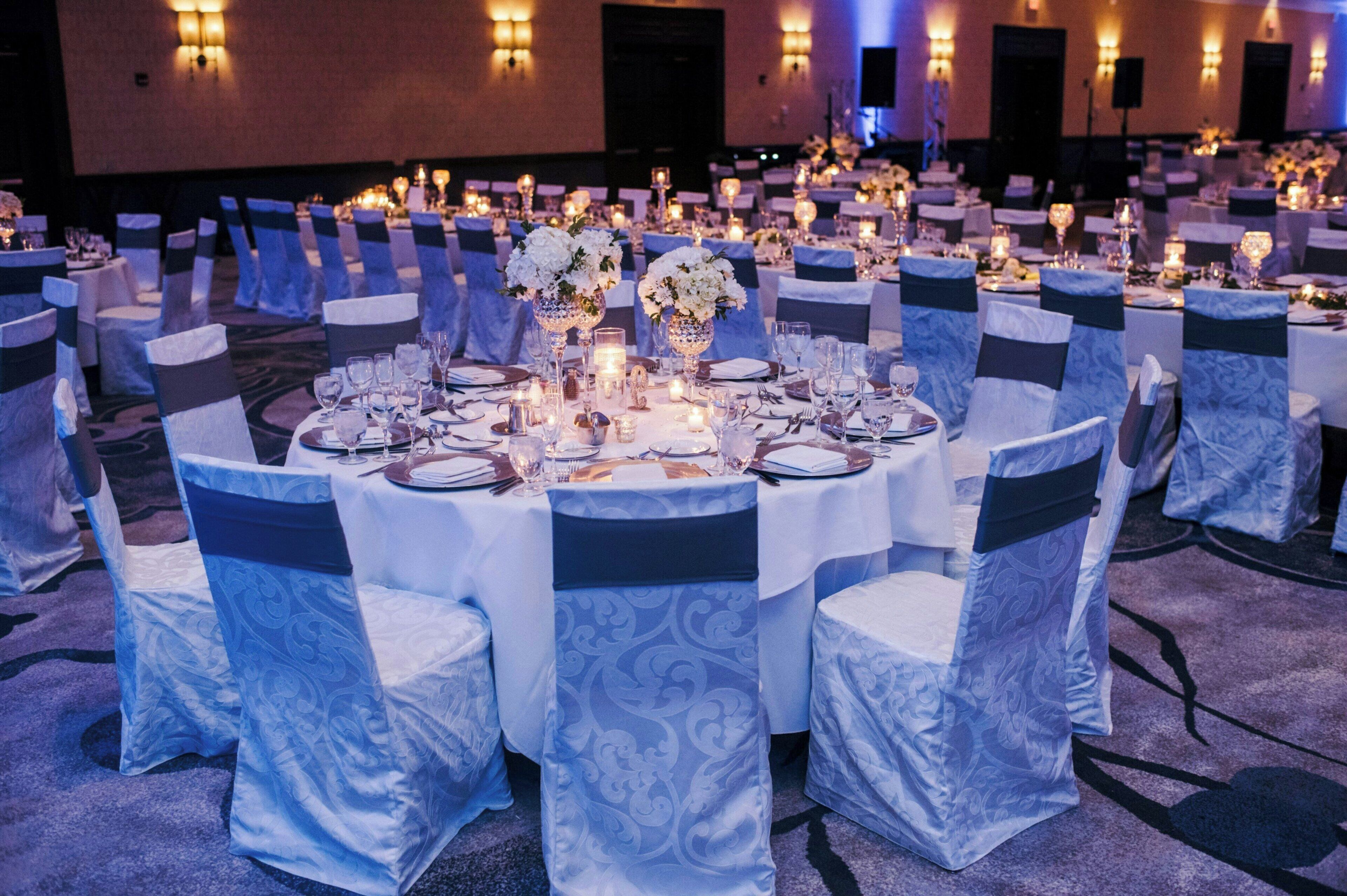 A banquet hall with round tables, chairs with blue sashes, and candle centerpieces.