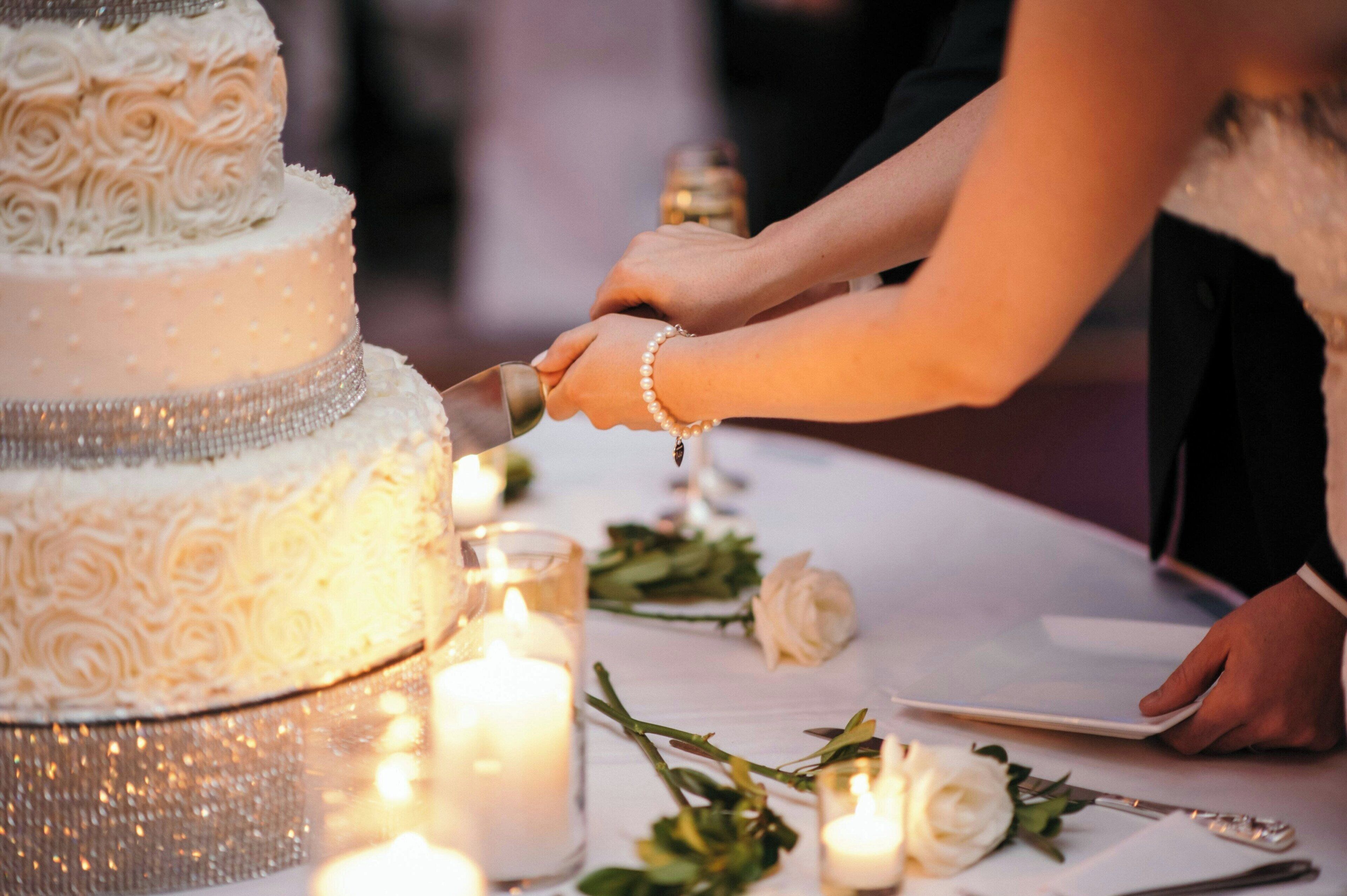 Un pastel de bodas con elaborados diseños de glaseado, una pareja cortándolo y velas sobre la mesa.