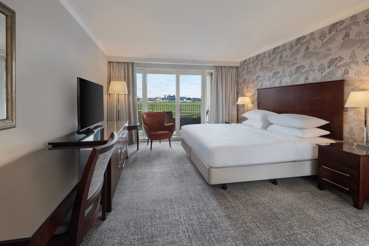 Une chambre d’hôtel avec un grand lit, un bureau avec une télévision, une chaise et une vue sur un champ verdoyant par la fenêtre.