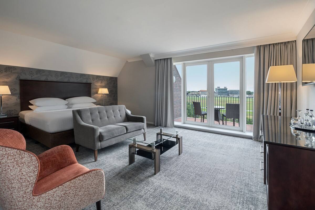 Une chambre d’hôtel avec un lit, un canapé gris, une table basse et une vue sur l’extérieur.