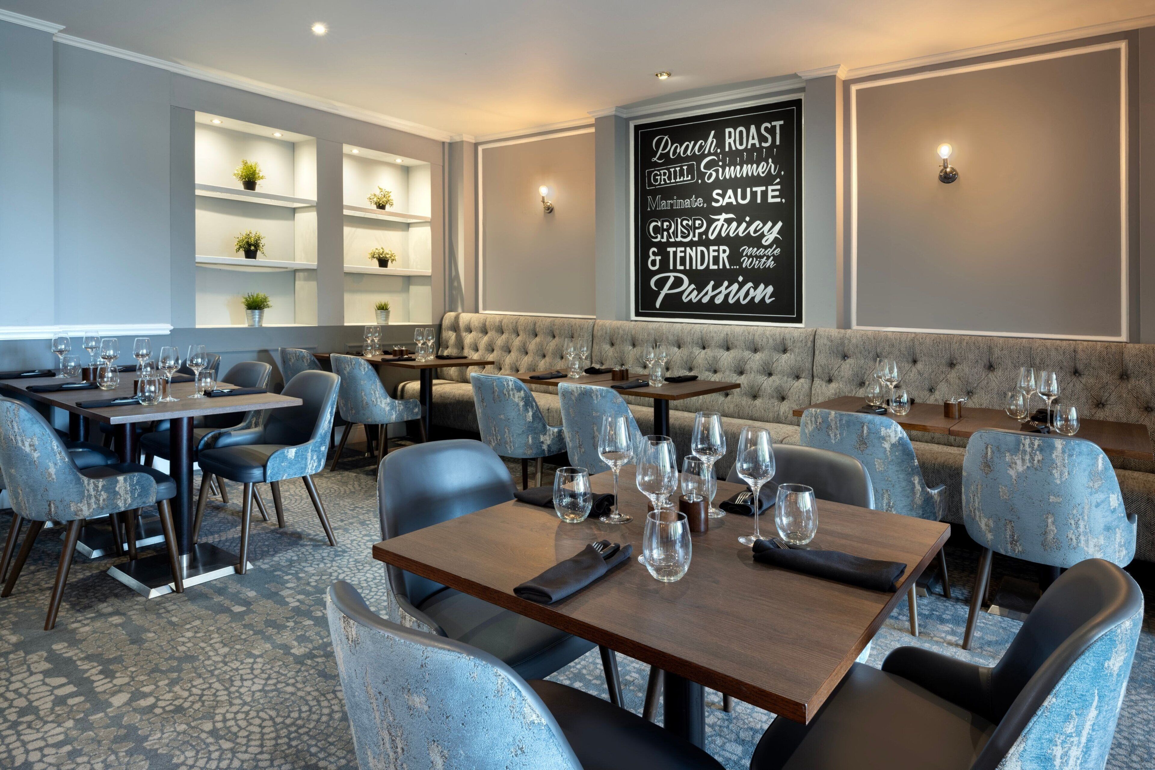 A modern dining area with a mix of booths and tables, each set with wine glasses and cutlery.