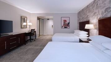 A hotel room with a large bed, a desk with a chair, a television, and a painting on the wall.