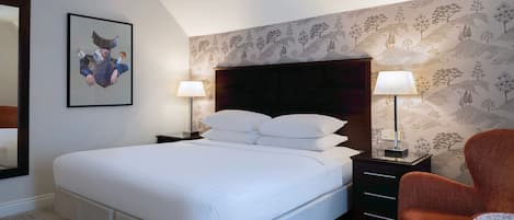 Une chambre d’hôtel bien aménagée, avec un grand lit, deux tables de chevet avec des lampes, une chaise et une œuvre d’art encadrée au mur.