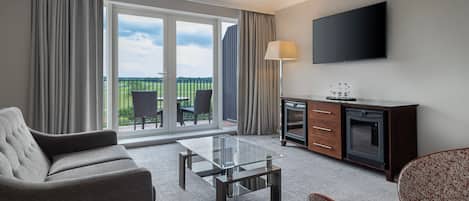 Habitación de hotel moderna con sofá, una mesita de cristal, televisión y vistas al exterior.