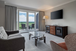 A modern hotel room with a sofa, a glass coffee table, a TV, and a view of the outdoors. - Delta Hotels by Marriott York (York)