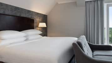 Habitación de hotel con una cama grande, una silla, una lámpara y vistas al exterior.
