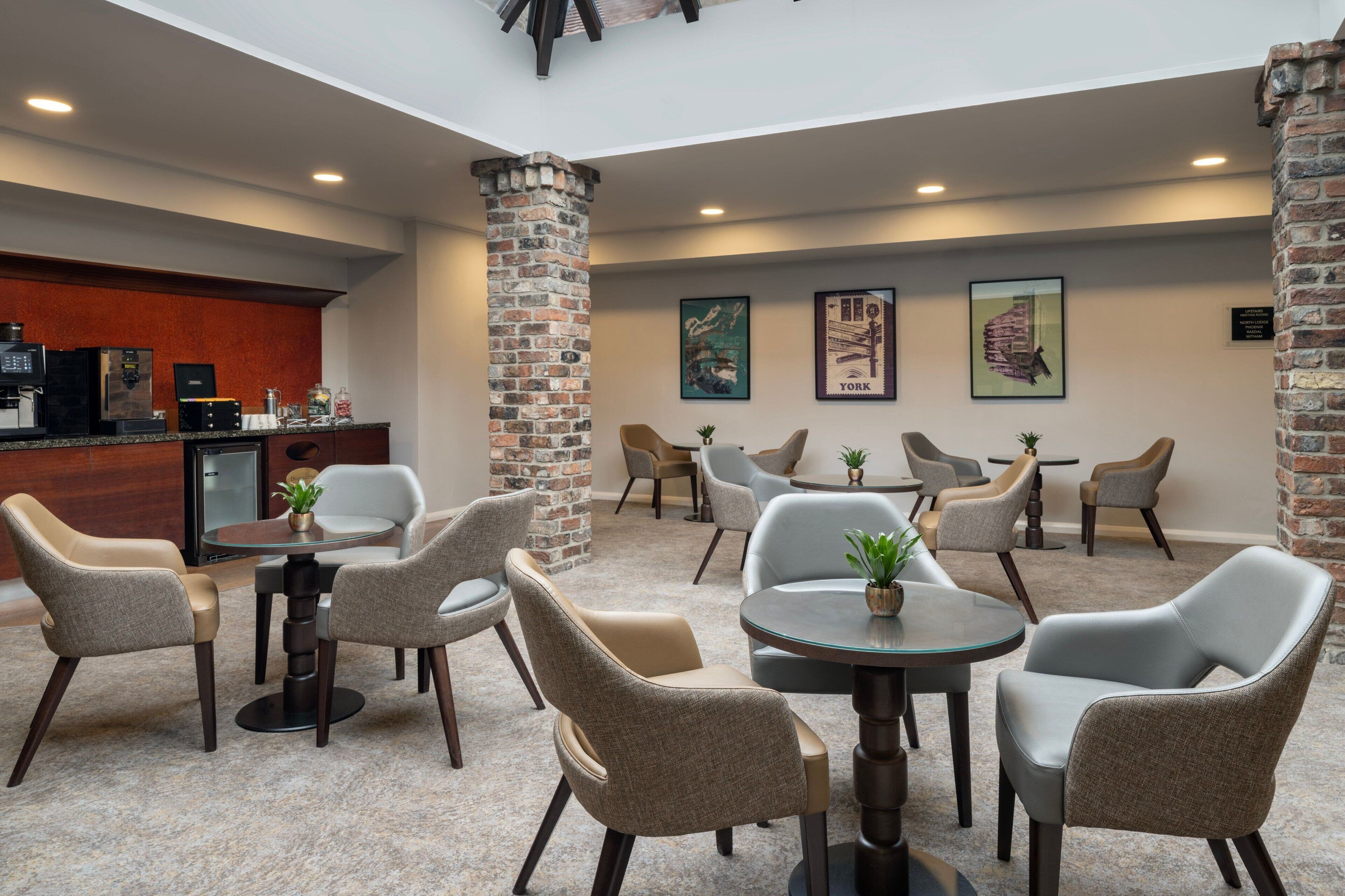 Eine Hotlellobby mit einer Kaffeebar, einer Sitzgelegenheit mit runden Tischen und Stühlen sowie dekorativer Wandkunst.