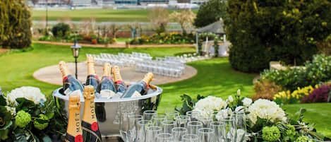 Una mesa con botellas de champán y copas, rodeada de follaje y flores.