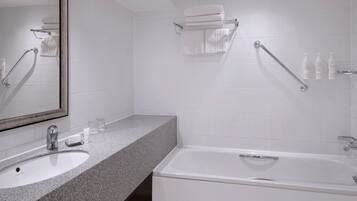 Une salle de bain moderne avec un lavabo surmonté d’un plan de travail en granit, un grand miroir, une baignoire blanche et un porte-serviettes.