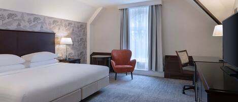 A hotel room with a large bed, a desk, a chair, and a TV.