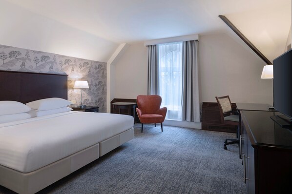 A hotel room with a large bed, a desk, a chair, and a TV.