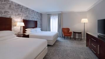 Ein Hotelzimmer mit zwei Betten, einem Fernseher, einem Schreibtisch und einem Sessel.