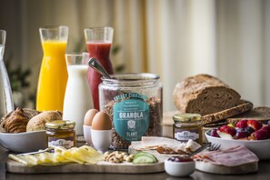 Una mesa de desayuno con diversos alimentos, como pan, huevos, frutas y un tarro de granola.