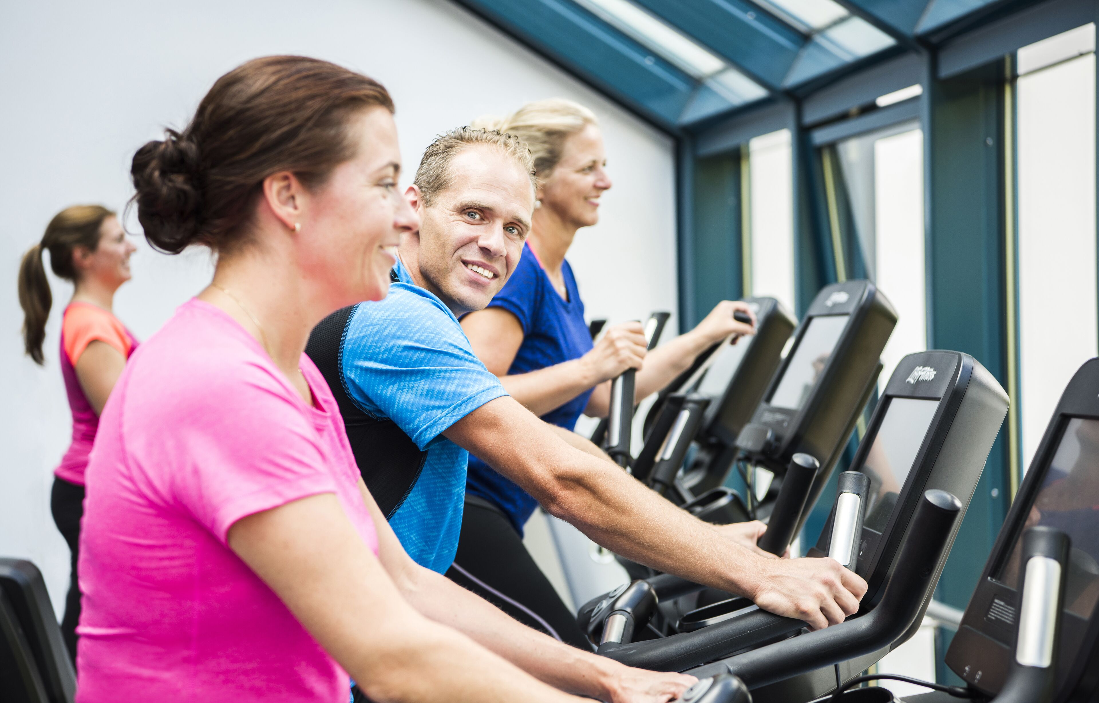 Un grupo de personas ejercitándose en cintas de correr en un gimnasio con amplias ventanas y diseño moderno.