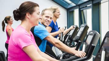 Un grupo de personas ejercitándose en cintas de correr en un gimnasio con amplias ventanas y diseño moderno.