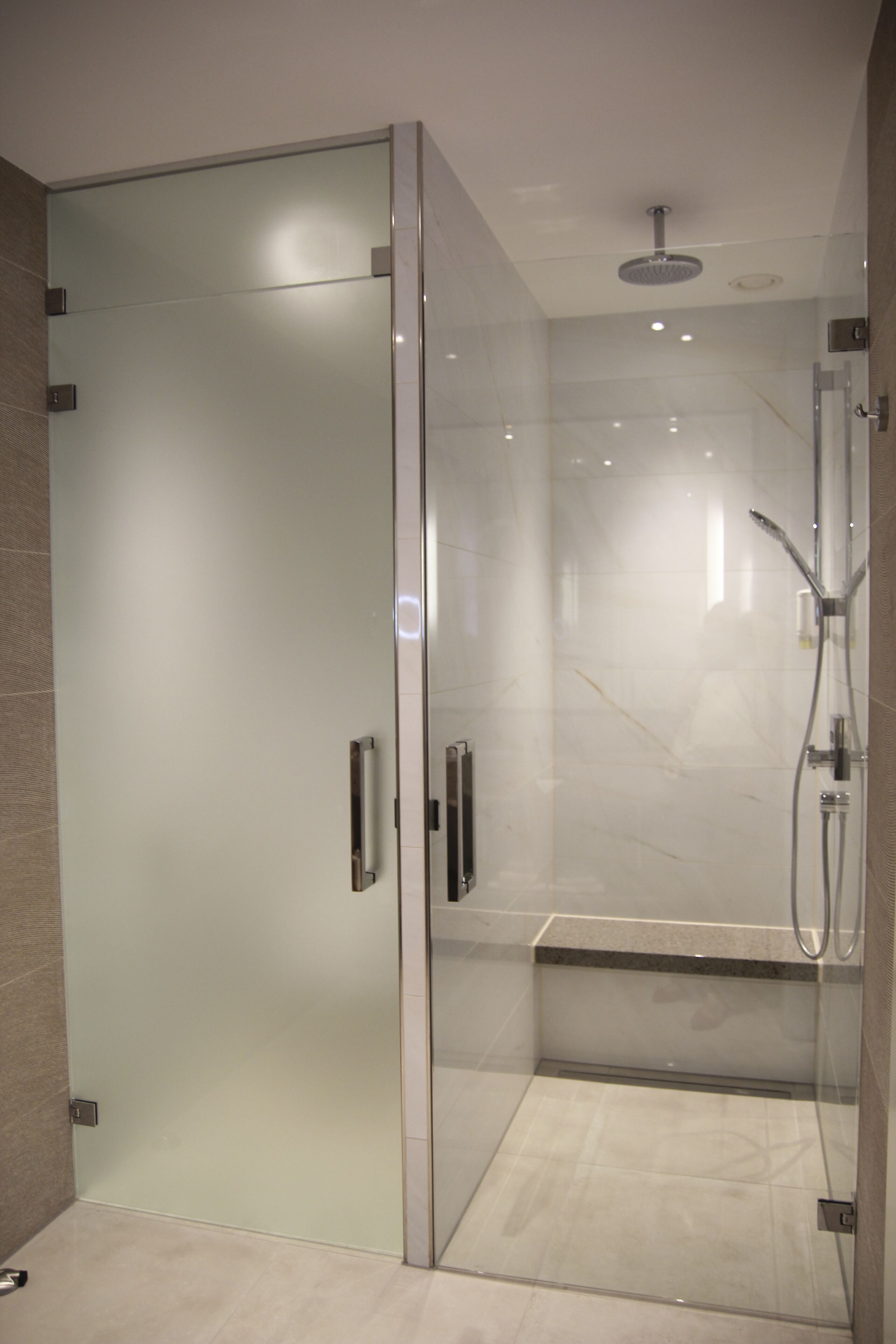 Un baño moderno con ducha envuelta en vidrio, un banco y un panel de control a la vista.