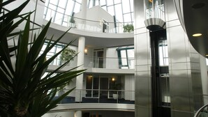 A multi-level atrium with glass railings, a central elevator, and potted plants.
