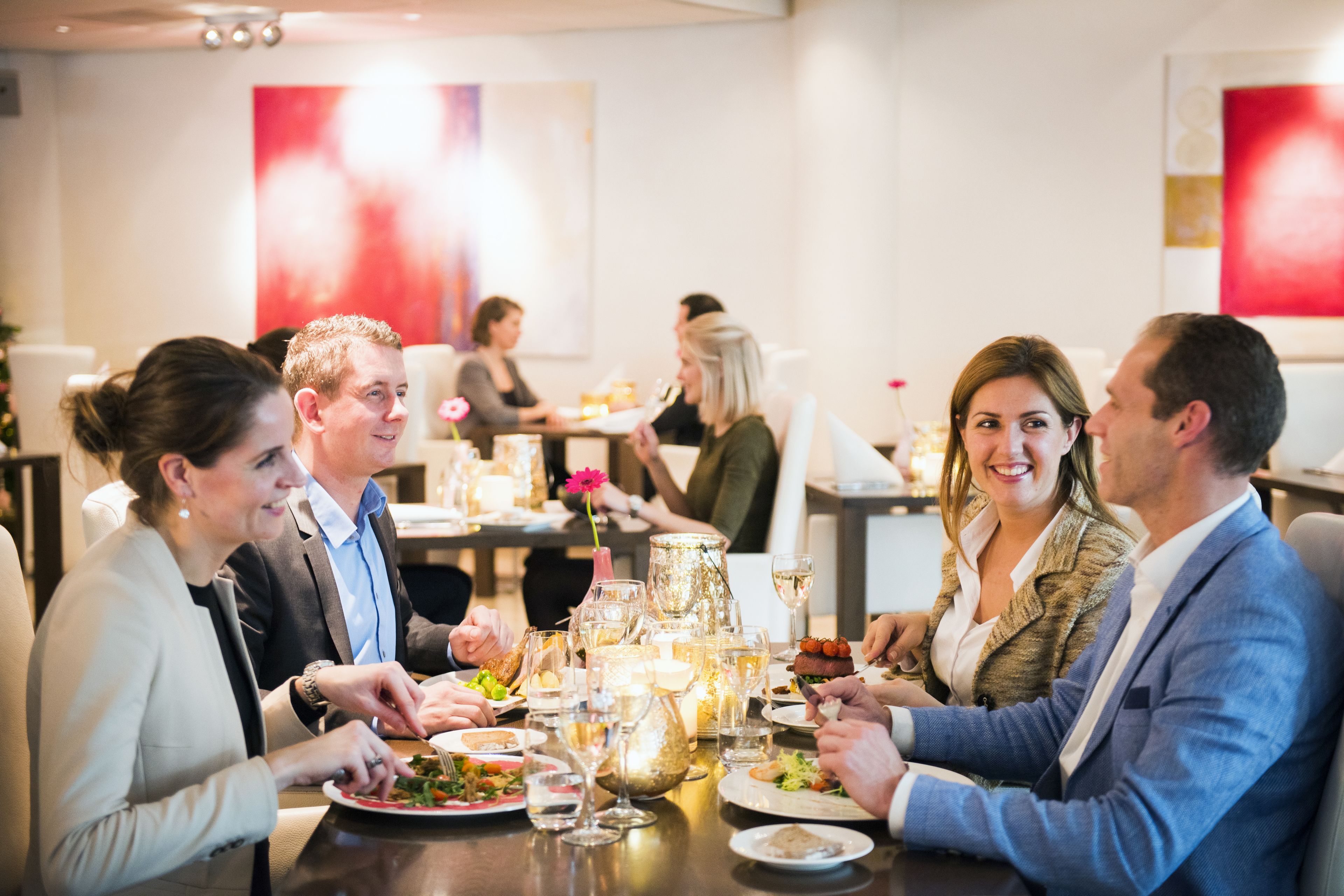 A group of people dining at a restaurant with a modern interior, featuring a table set with various dishes and drinks.